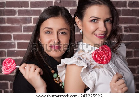 Closeup portrait of two young girlfriend girls with lollipops. Happy and cheerful teens. Red lips and hearts. Valentine\'s day concept.