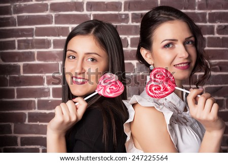 Closeup portrait of two young girlfriend girls with lollipops. Happy and cheerful teens. Red lips and hearts. Valentine\'s day concept.