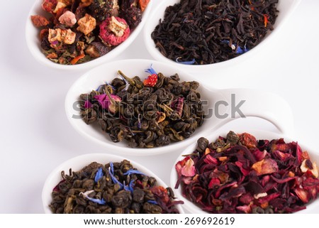 Dry tea in white bowls, on white background. Leaves of red, green and black tea. Macro photo.