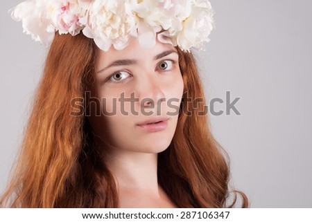 Beautiful close-up portrait of a woman with peonies wreath. Spring care concept. Natural look. Long red hair.