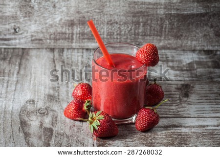 A glass of fresh strawberry smoothie on a wooden background. Summer drink and refreshment organic concept.