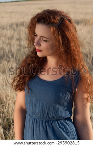 Beautiful woman enjoying in the nature in a field of barley and wheat. Long red hair concept. red lipstick.