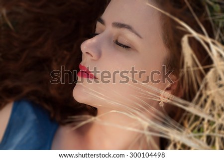Beautiful woman enjoying in the nature in a field of barley and wheat. Long red hair concept. red lipstick.