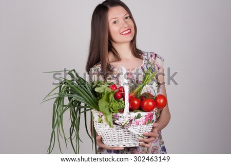 Close-up portrait of a young woman with a basket of fresh vegetables. Happy girl with carrots, reddish, onion and tomato. Vitamins and minerals. Healthy food concept. Grocery.