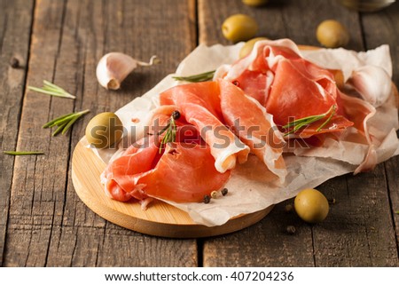 closeup of thin slices of prosciutto with mixed olives and paprika on wooden cutting board
