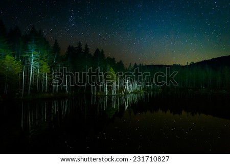 Stars in the night sky reflecting in Deception Pond at night, in White Mountain National Forest, New Hampshire.
