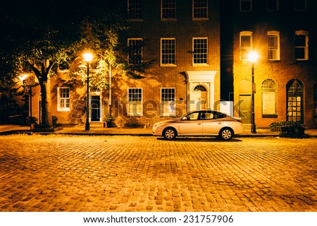 Parked car in front of brick buildings on a cobblestone street at night in Fells Point, Baltimore, Maryland.