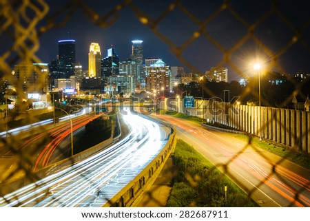 Chain link fence and view of I-35 and the skyline at night, seen from the 24th Street Pedestrian Bridge, in Minneapolis, Minnesota.