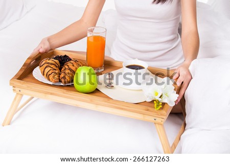 Woman holding wood tray with coffee, orange juice, apple croissant in bed in the morning