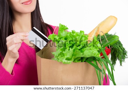 Beautiful young woman with credit card holding paper bag with groceries from grocery shop