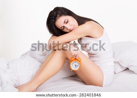 Tired young woman holding alarm clock in bed in the morning