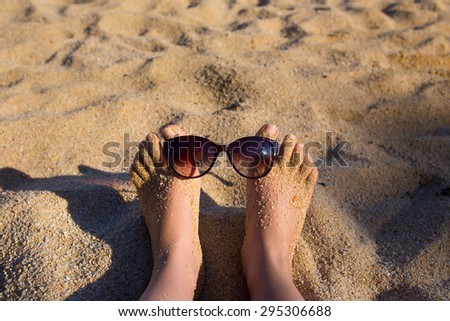 Luxury young woman legs and feet sunbathing on beach wearing sun glasses.