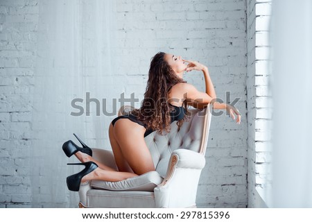 Perfect, sexy body, legs and ass of young woman wearing seductive black lingerie. Beautiful hot female in bodysuit posing on luxury vintage chair.