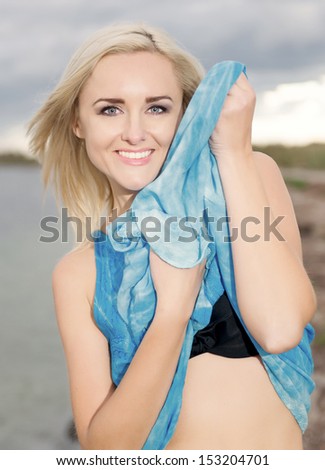 the happy, young and beautiful girl costs on a beach and holds a blue dress