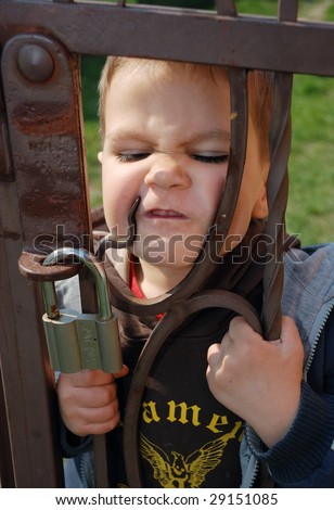 a little boy writhes ugly faces at a fence