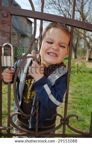 a little boy writhes ugly faces at a fence