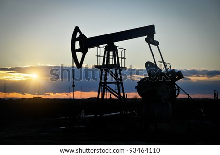 Oil field pump jack silhouette with setting sun Oil field pump jack silhouette with setting sun