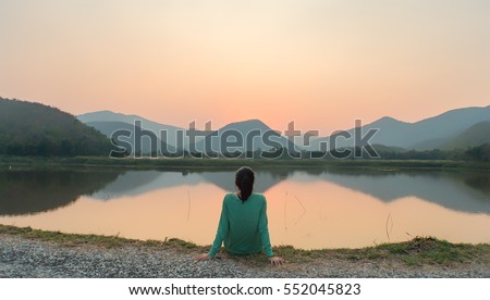 A woman is sitting at ease by the lake during sunset moment.