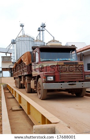 Truck on a scale with a load of soybeans in Brazil, soy storage warehouse and silos in the background