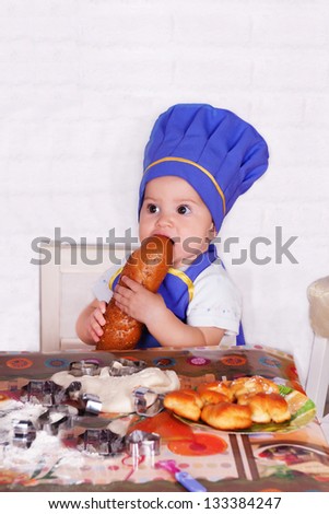 adorable baby cooking in kitchen. little cute child in costume of Cook. funny child in costume of the Cook eats bakery products