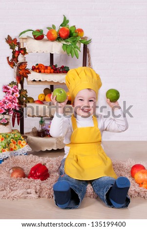 adorable baby cooking in kitchen. little cute child in costume of Cook. the happy nice small child in the costume of the cook with a pan. Baby cook with vegetables in studio