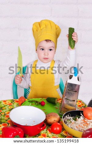 adorable baby cooking in kitchen. little cute child in costume of Cook. the happy nice small child in the costume of the cook with a pan. Baby cook with vegetables in studio