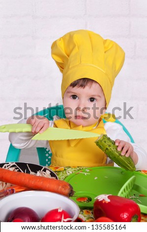 adorable baby cooking in kitchen. little cute child in costume of Cook. little boy in a suit of the cook in the kitchen preparing soup.