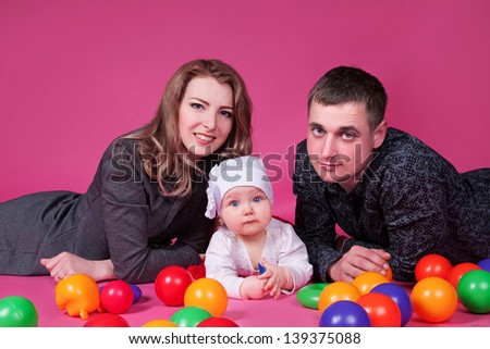 Happy family with  child - beautiful mother and father hug their daughter, posing on pink background in studio closeup