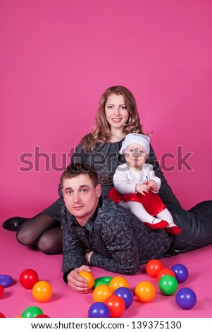 Happy family with  child - beautiful mother and father hug their daughter, posing on pink background in studio closeup