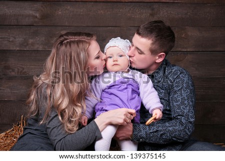 Happy family with  child - beautiful mother and father hug their daughter, posing on hay in studio closeup