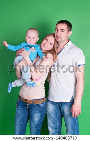 Happy family with the child  - beautiful mother and father hug their son, posing on green background in studio closeup