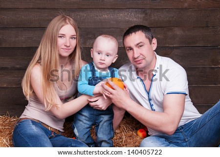Happy family with the child - beautiful mother and father hug their son, posing on hay in studio closeup