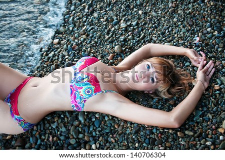 alluring sexy woman relaxing and posing on beach in swimwear and golden jewelry. Beautiful happy girl enjoying hot summer sun. Romantic slim lady at vacation near the sea. Pinup bikini model resting