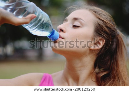 Young woman stretching in the park and drinking water before Exercise. Caucasian sport fitness model in city park outdoors.