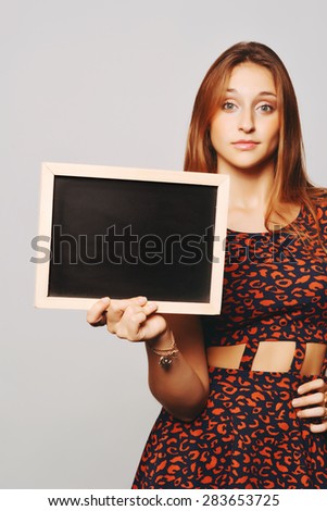 Beautiful young woman holding and showing something on a chalkboard