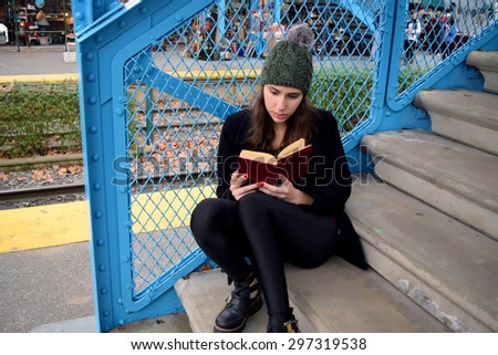 Latin woman reading a book on the stairs of the train station. Autumn fashion. Fall season.