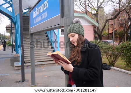 Latin woman reading on the train station. Autumn fashion. Fall season.