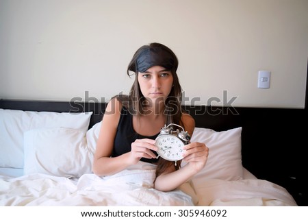 Sleepy young woman in bed after waking up, holding an alarm clock