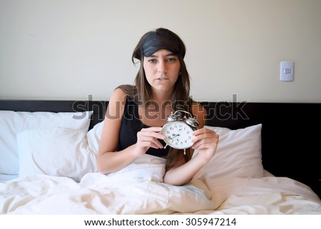 Sleepy young woman in bed after waking up, holding an alarm clock