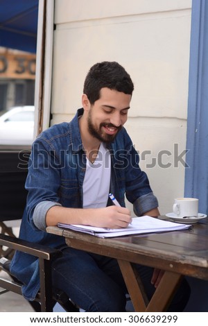 Young latin man studying at an outdoor cafe. Urban style.