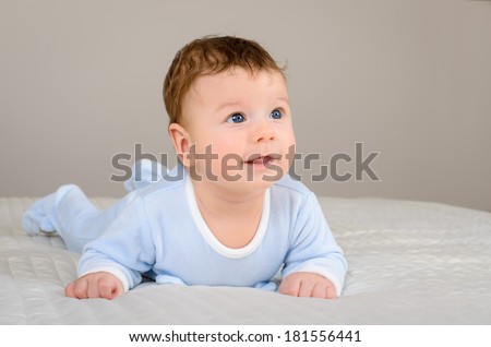 Cute smiling baby boy in bed lying on his belly and looking at the side of camera