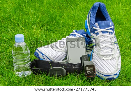Modern sport equipment for running on the grass. Sneakers, water, smartphone, sport watch and heart sensor
