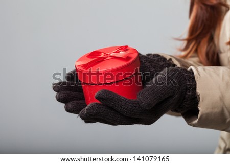 Close-up of woman hands carrying a small round red gift box wearing gloves