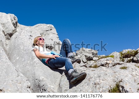Pretty young woman resting during the hike laying on large boulders and enjoying the sun on a bright day