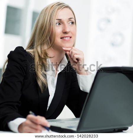 Businesswoman sitting thinking at her desk in front of her laptop computer and staring into the distance