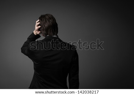 Dark studio portrait of a serious man standing in the shadows with his arms folded and a pensive expression