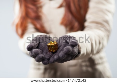 Woman holding a tiny giftwrapped little gift box carefully cupped in her gloved hands as she offers it to a loved one