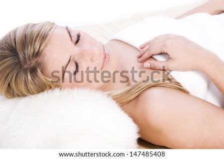 Beautiful young blond woman relaxing sleeping on her back with a serene expression and her head resting on a fluffy pillow as she dreams sweet dreams