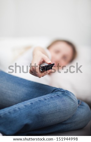 Woman lying in bed with a remote control in her hand extended towards the viewer as she changes the television channel
