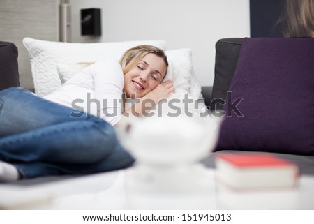 Beautiful young woman sleeping in bed taking a midday nap curled up on top of the bed with a serene smile on her face as she enjoys her dreams